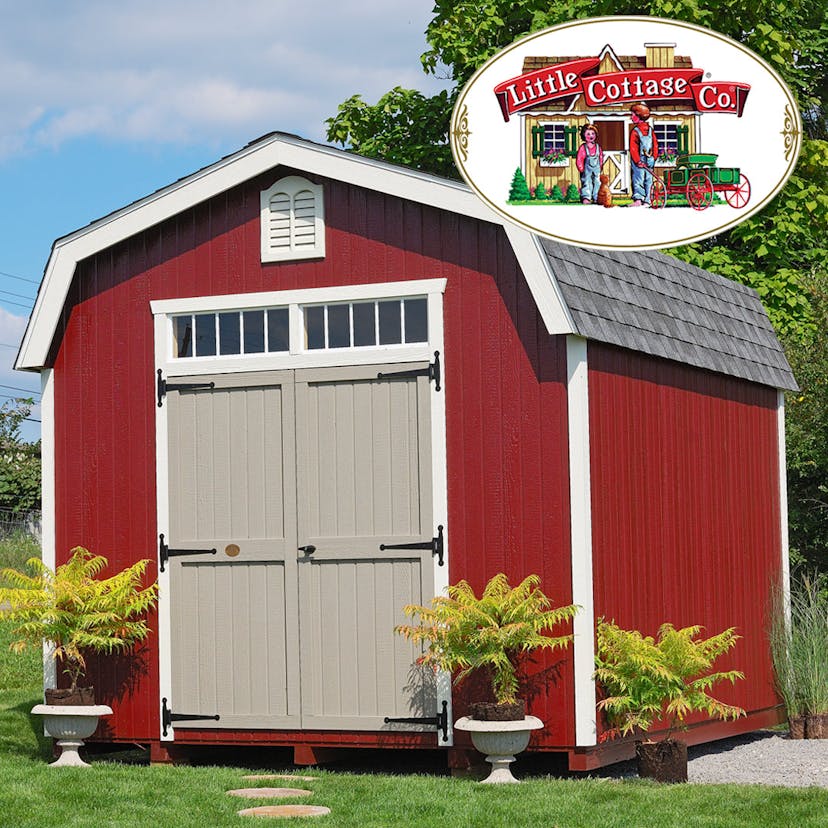 Red Colonial Woodbury barn shed in backyard with stone pathway and potted plants beside it.